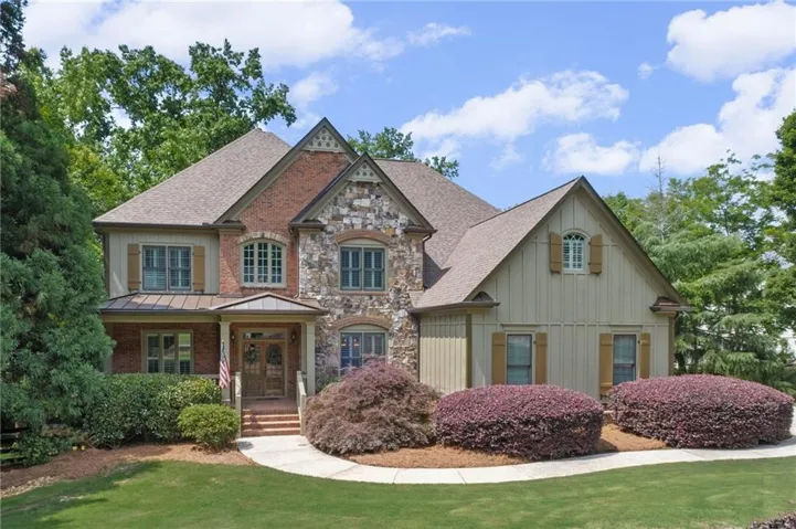 Expansive residence featuring a brick and stone facade, multiple gables, a covered front entry, architectural shingles, and mature landscaping