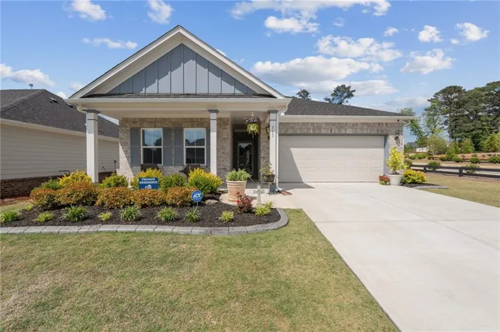 Modern ranch-style home featuring a mixed-material facade, an attached two-car garage, a covered front porch, a concrete driveway, and established landscape beds