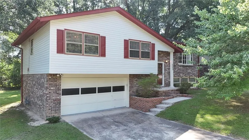 Split-level residence featuring a brick and white siding exterior, red window shutters, an integrated garage, and a concrete pathway leading to the main entrance