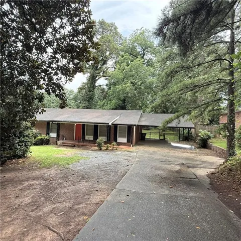 Brick facade ranch home featuring an attached carport, covered front porch, and a paved driveway
