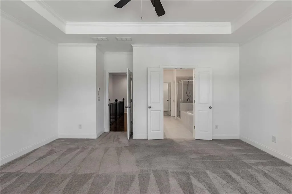 Unfurnished bedroom featuring a raised ceiling, carpet, ornamental molding, and a ceiling fan