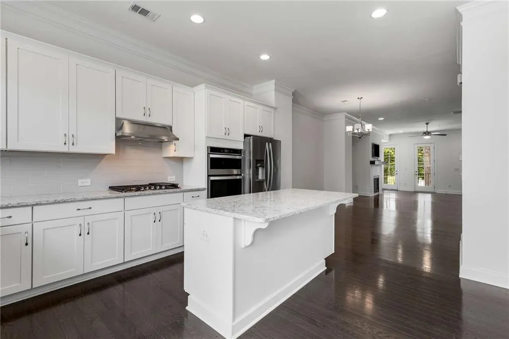 Kitchen with stainless steel appliances, under cabinet range hood, recessed lighting, white cabinets, and tasteful backsplash