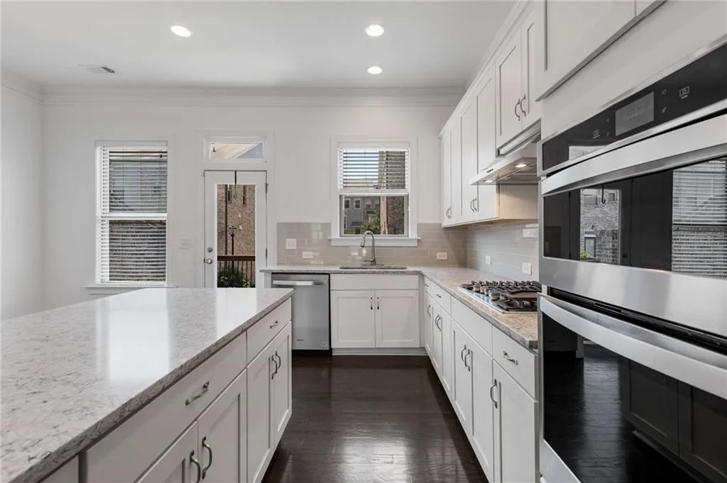 Kitchen with stainless steel appliances, crown molding, white cabinets, decorative backsplash, and light stone countertops