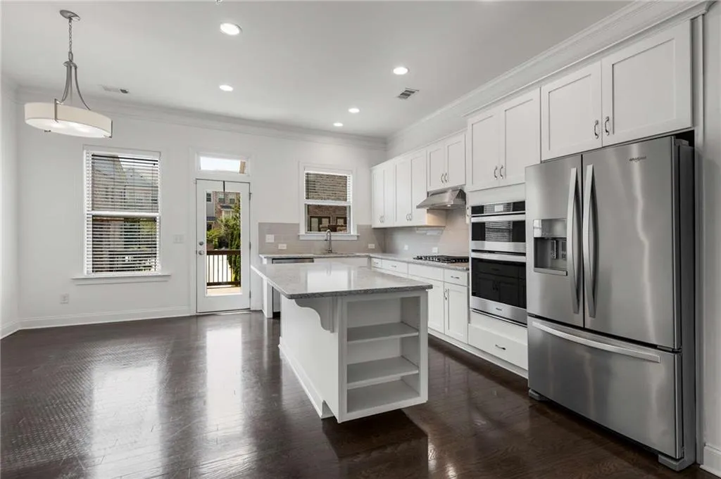 Kitchen featuring appliances with stainless steel finishes, under cabinet range hood, crown molding, open shelves, and white cabinetry