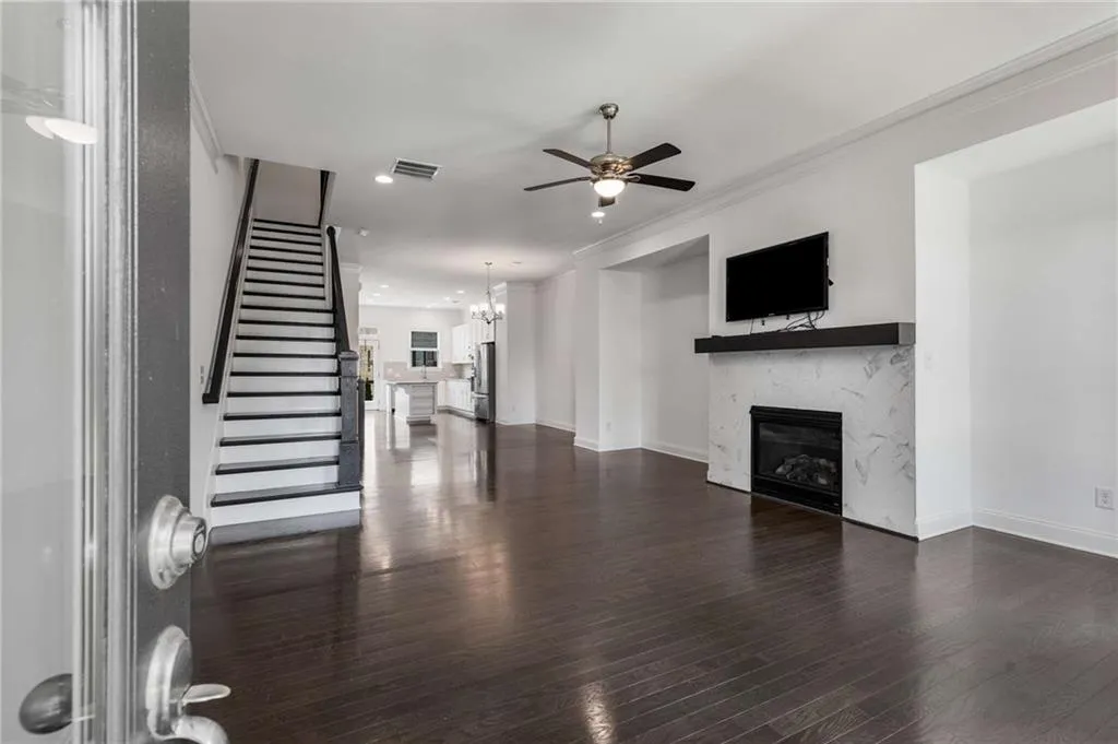 Unfurnished living room with ceiling fan, a glass covered fireplace, ornamental molding, dark wood-style floors, and stairway