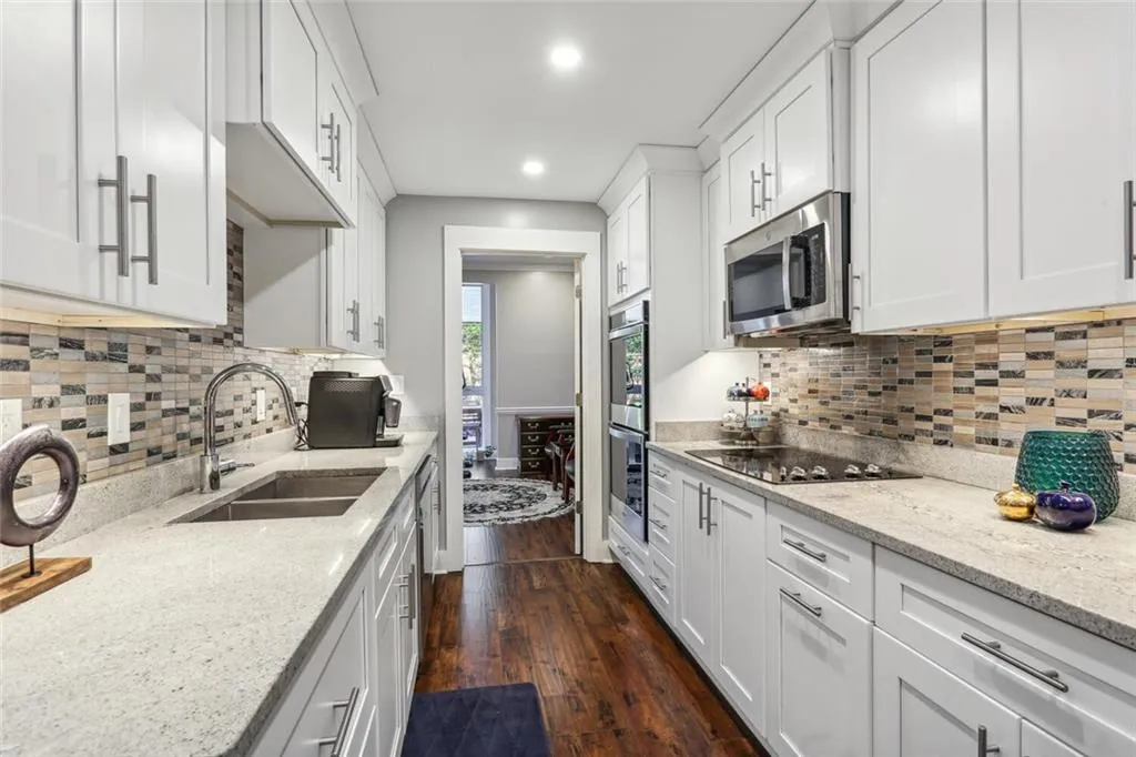 Kitchen with sink, dark wood-type flooring, white cabinetry, black electric stovetop, and light stone countertops
