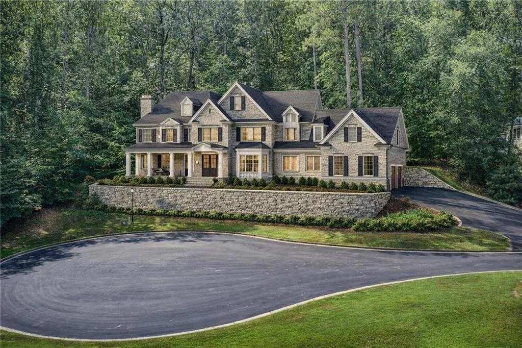 View of front of property with a porch, a chimney, stone siding, asphalt driveway, and a wooded view