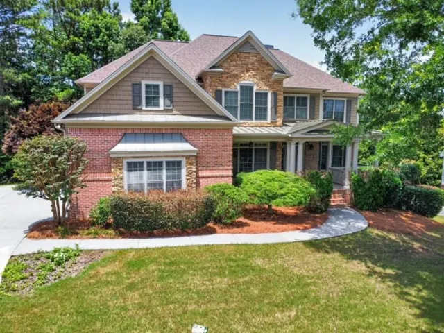 Brick and stone facade residence featuring a covered front porch with columns, gabled rooflines, decorative window shutters, and mature landscaping