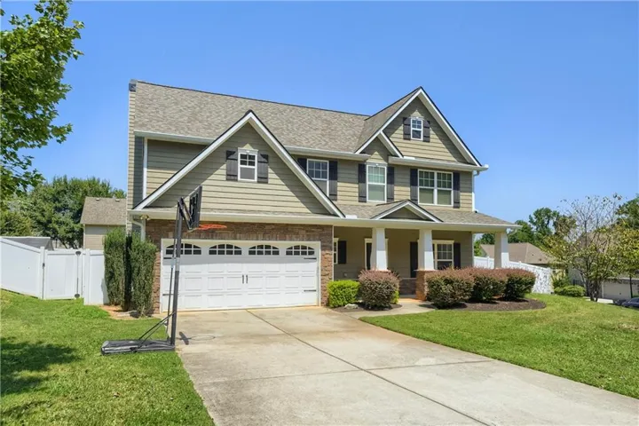 Two-story property featuring a front porch, a two-car garage, and a fenced side yard