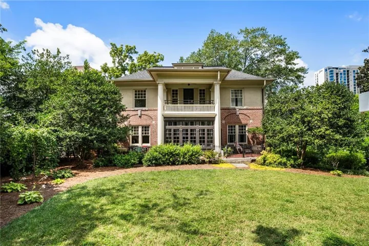Brick and stucco exterior featuring a columned portico, upper-level balcony with iron railing, and lower-level French doors