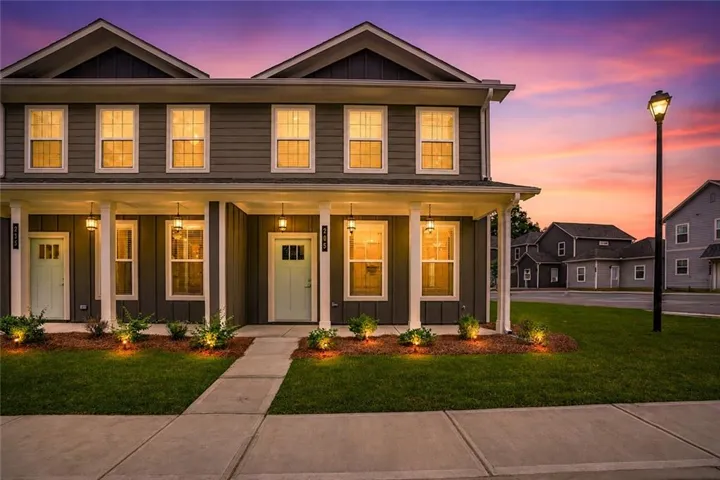 Modern townhome exterior with horizontal siding, a covered porch with white columns, light blue entry doors, and ground-level landscaping with accent lighting