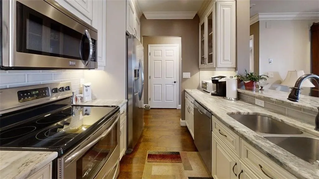 Kitchen featuring appliances with stainless steel finishes, crown molding, glass insert cabinets, dark wood-style floors, and decorative backsplash