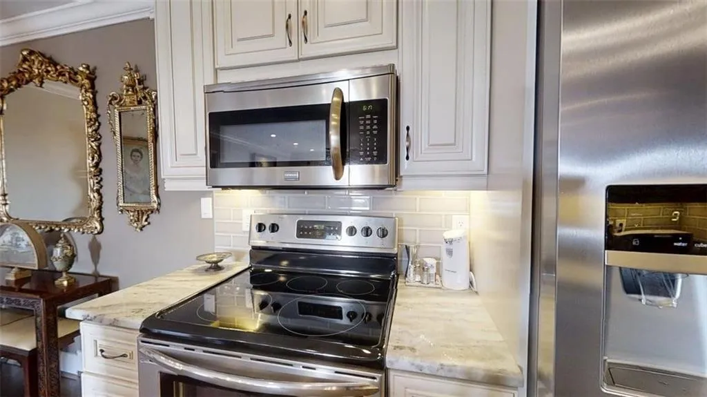 Kitchen with appliances with stainless steel finishes, tasteful backsplash, light stone countertops, and white cabinets