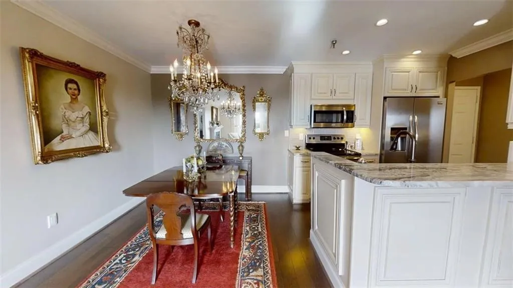 Kitchen with dark wood-style flooring, appliances with stainless steel finishes, a chandelier, light stone counters, and ornamental molding