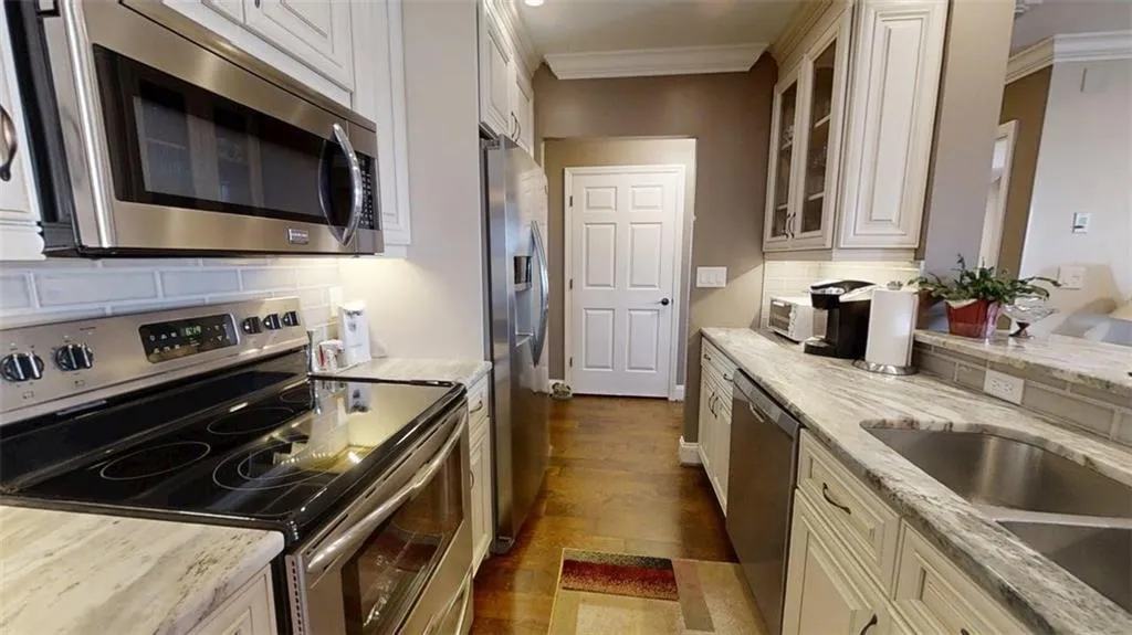Kitchen with stainless steel appliances, ornamental molding, tasteful backsplash, glass insert cabinets, and dark wood finished floors
