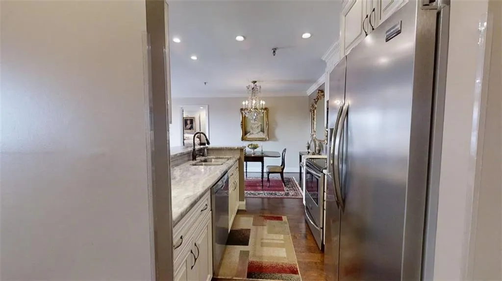 Kitchen featuring stainless steel appliances, crown molding, white cabinets, light stone counters, and a chandelier
