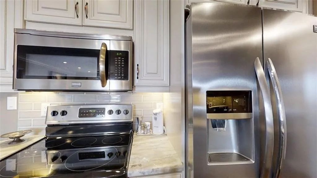 Kitchen with appliances with stainless steel finishes, decorative backsplash, and light stone counters