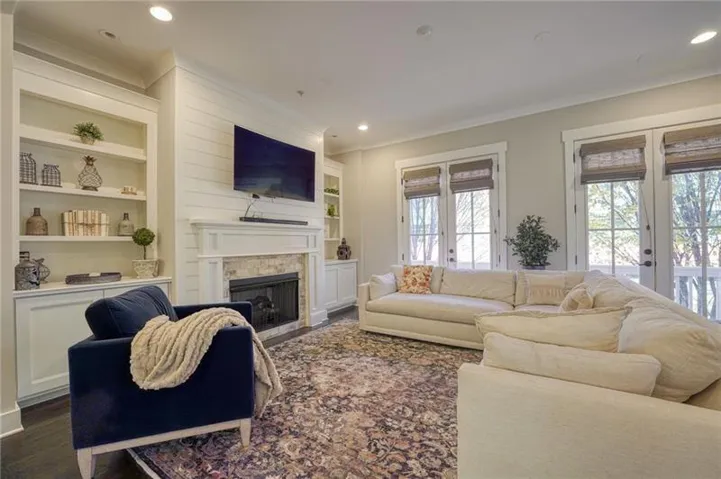 Living area with a stone-surround fireplace, shiplap accent wall, built-in shelving, and dark wood-finish flooring