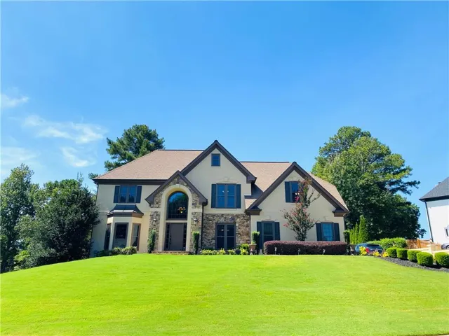 Stucco and stone exterior with a prominent arched entry, multiple gables, manicure lawn