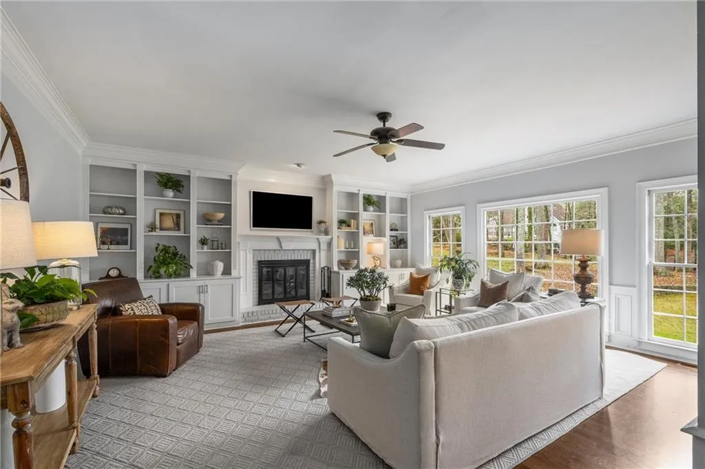 Living area with crown molding, a ceiling fan, a fireplace, wood finished floors, and built in features