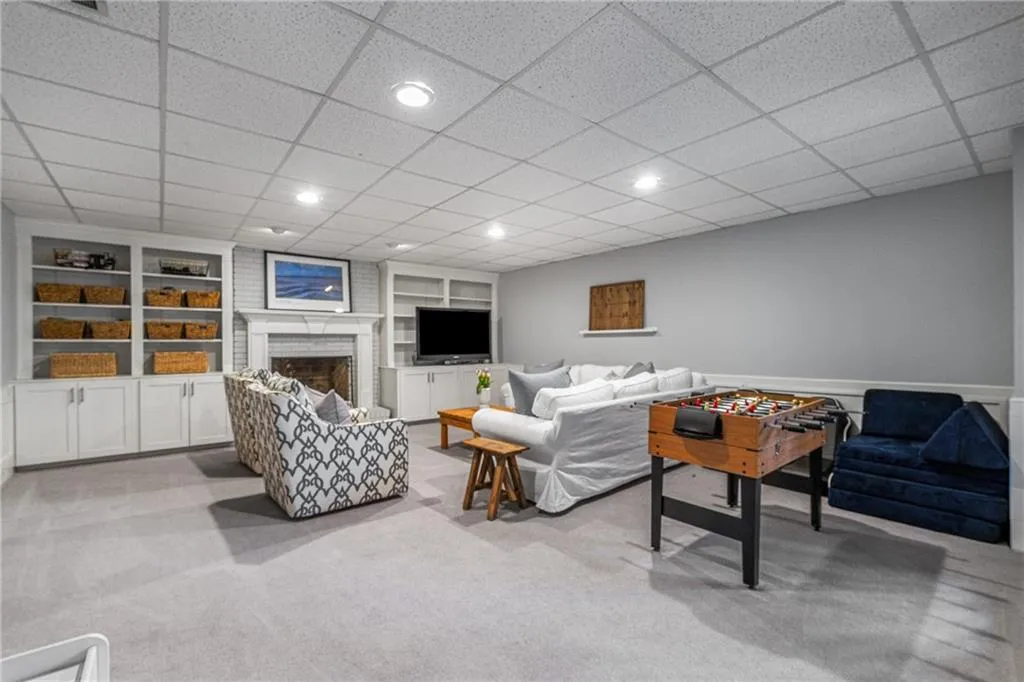 Living room with built in features, recessed lighting, a brick fireplace, and light colored carpet