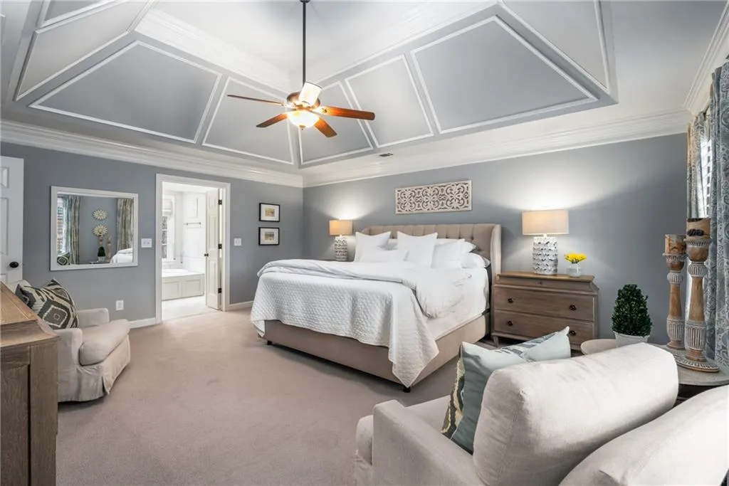 Bedroom featuring coffered ceiling, light colored carpet, ornamental molding, baseboards, and ensuite bathroom