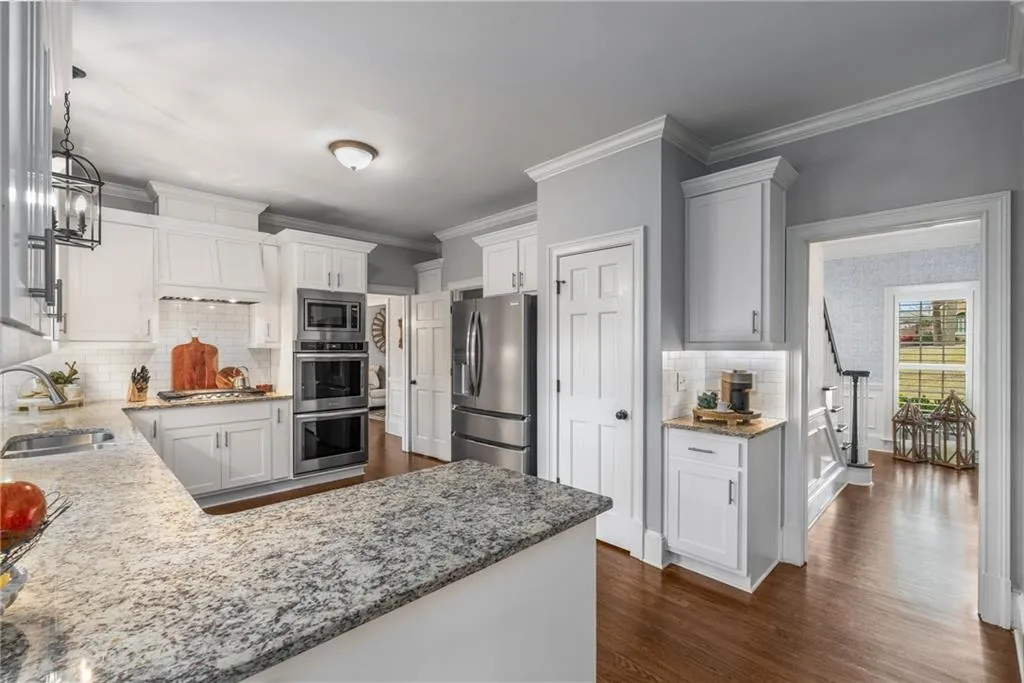 Kitchen featuring dark wood-type flooring, a sink, stainless steel appliances, and light stone counters