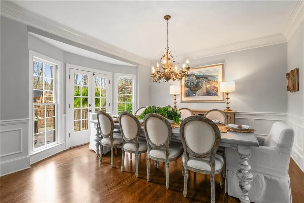 Dining area with a wainscoted wall, french doors, wood finished floors, ornamental molding, and an inviting chandelier