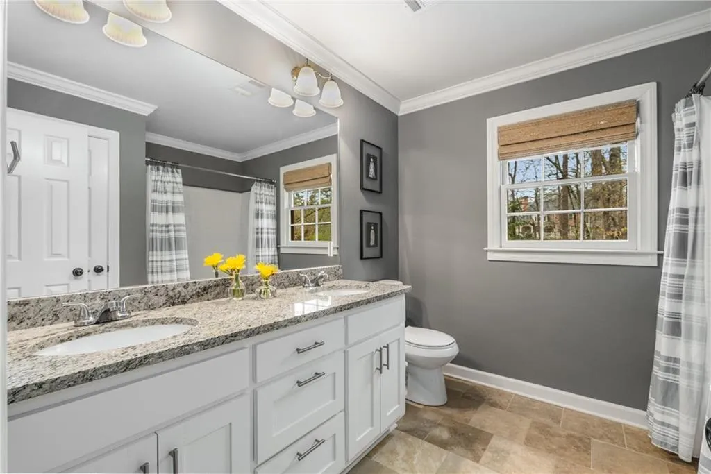 Full bath with double vanity, a sink, toilet, and baseboards