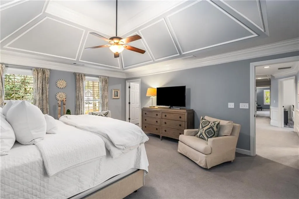 Bedroom featuring ornamental molding, coffered ceiling, a ceiling fan, and light carpet