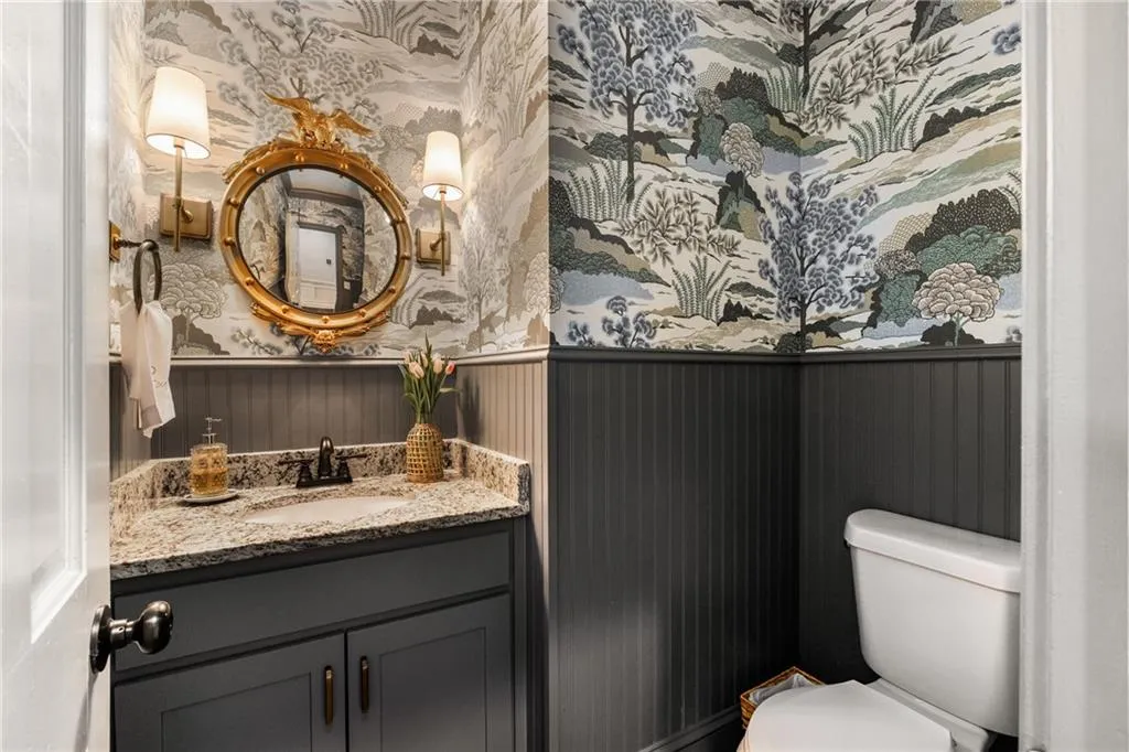 Half bathroom with wallpapered walls, toilet, vanity, and wainscoting