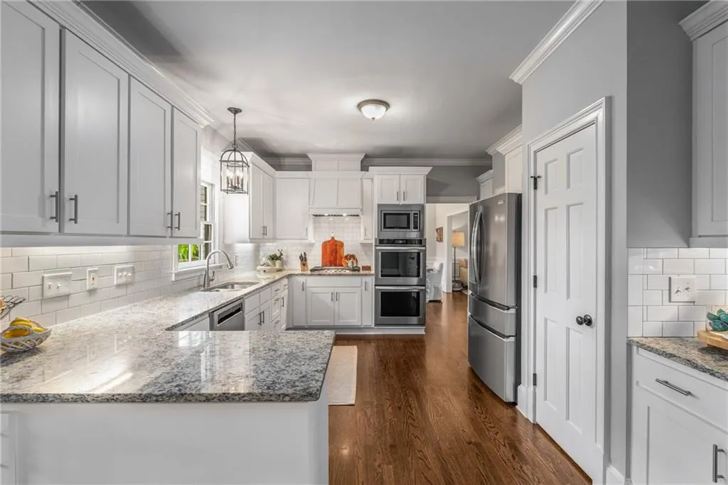Kitchen with ornamental molding, light stone countertops, appliances with stainless steel finishes, dark wood-type flooring, and a sink