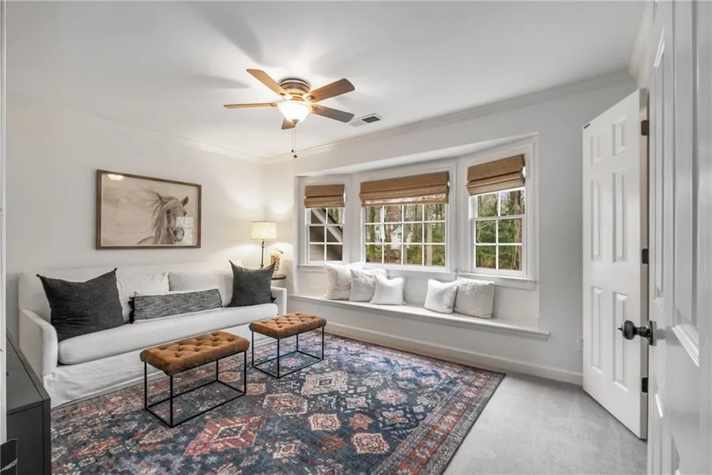 Living area with carpet flooring, ceiling fan, visible vents, and crown molding