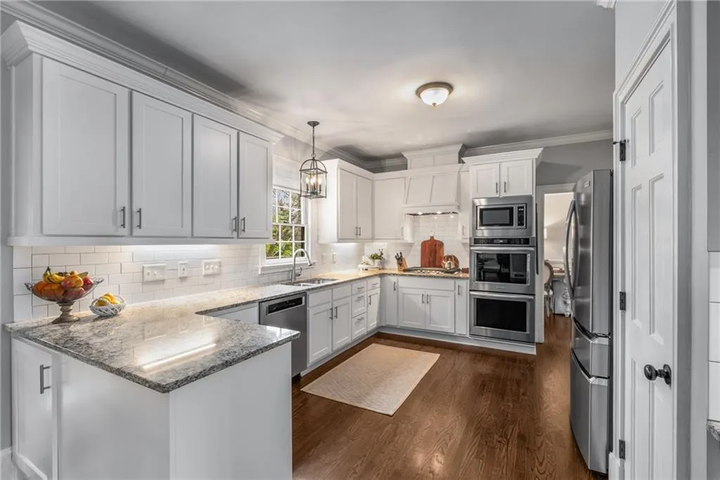 Kitchen featuring a peninsula, ornamental molding, stainless steel appliances, a sink, and dark wood-style floors