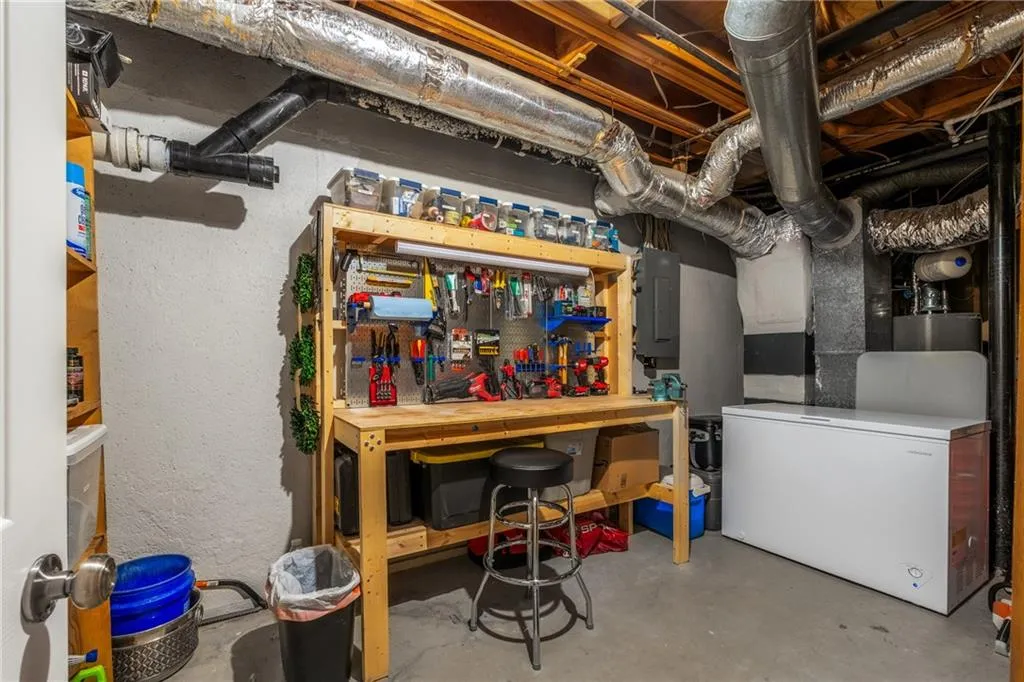 Unfinished basement featuring electric panel, white fridge, and a workshop area