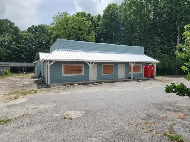 Commercial building featuring light blue siding, a white corrugated metal roof, and a covered porch supported by white columns