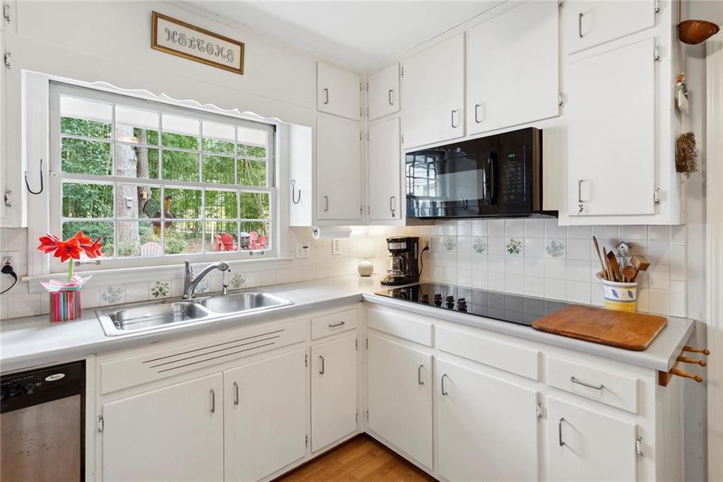 Kitchen featuring black appliances, light wood-type flooring, backsplash, white cabinets, and sink Kitchen featuring black appliances, light wood-type flooring, backsplash, white cabinets, and sink