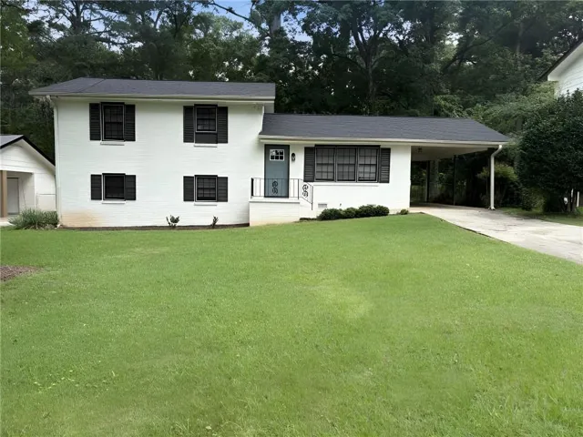 Two-story residence featuring a white brick exterior, black window shutters, a prominent front lawn, a covered carport, and a separate side garage structure