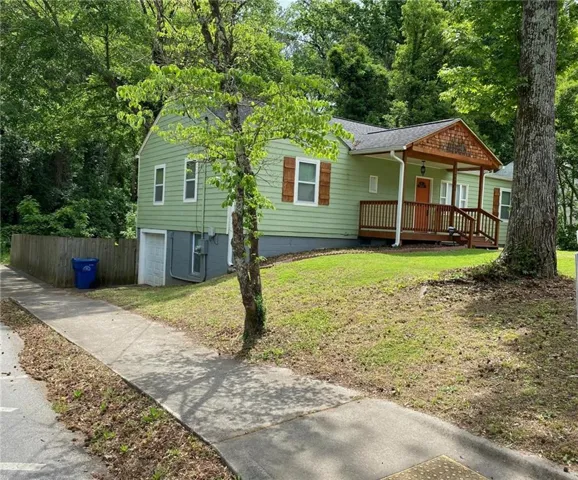 View of front facade with a front lawn, a porch, a garage, a shingled roof, and driveway