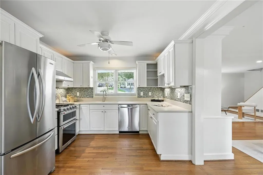 Kitchen with stainless steel appliances, under cabinet range hood, ceiling fan, light countertops, and wood finished floors