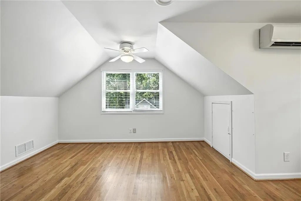 Additional living space with a wall mounted AC, ceiling fan, wood-type flooring, and vaulted ceiling