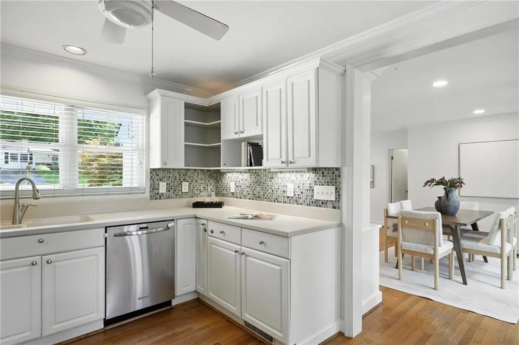 Kitchen featuring stainless steel dishwasher, open shelves, white cabinetry, decorative backsplash, and ornamental molding