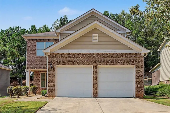 Brick facade with siding accents, attached two-car garage, concrete driveway, and mature landscaping