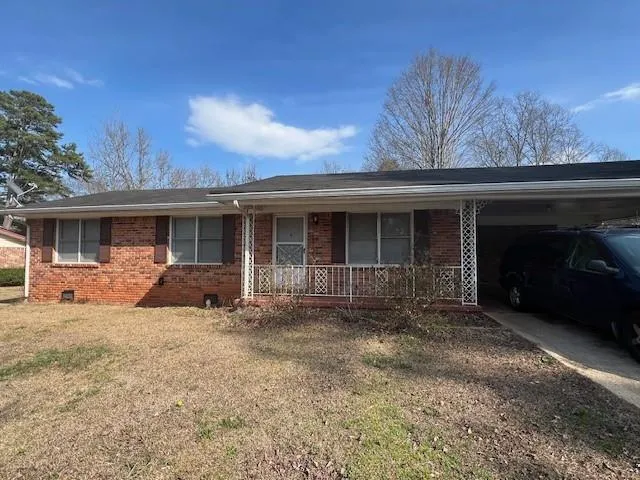 Ranch-style house with crawl space, brick siding, covered porch, a carport, and a front yard