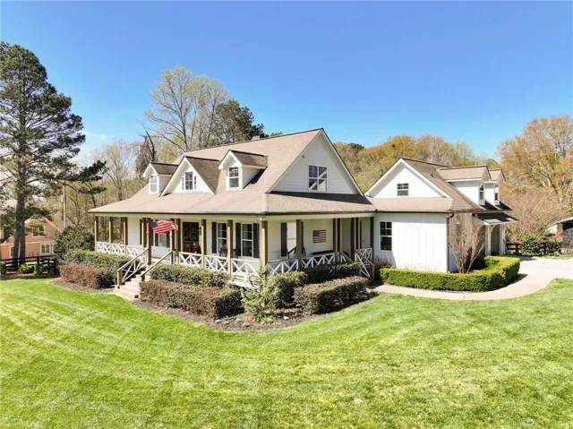 View of front facade with a porch, a front lawn, roof with shingles, and a garage