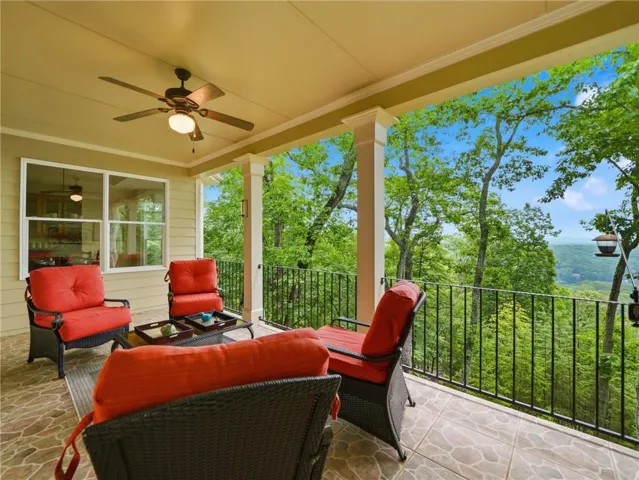 Expansive covered patio featuring a ceiling fan, stone tile flooring, painted columns, and a metal railing