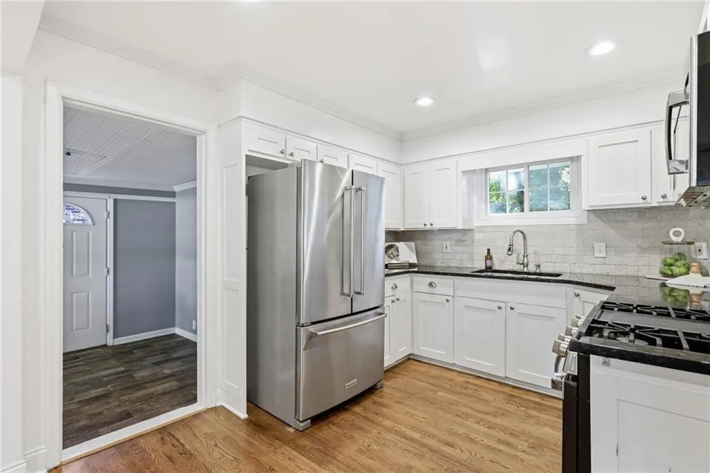 Kitchen featuring appliances with stainless steel finishes, ornamental molding, decorative backsplash, light wood-style flooring, and dark stone countertops