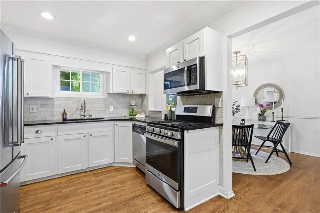 Kitchen featuring stainless steel appliances, decorative backsplash, crown molding, white cabinets, and light wood-style floors
