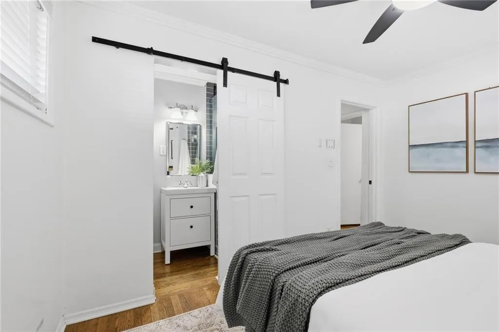 Bedroom with ornamental molding, wood finished floors, a barn door, connected bathroom, and ceiling fan