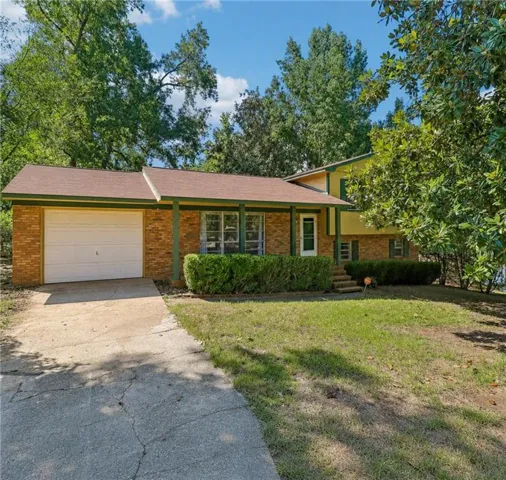 Brick exterior with an attached garage, covered front porch, and mature landscaping